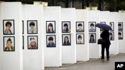 Seorang perempuan melihat karikatur para korban kapal feri Sewol yang tenggelam, di altar memorial di Ansan, Korea Selatan (16/4). (AP/Lee Jin-man)