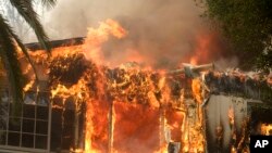 FILE - The Woolsey Fire burns a home in Malibu, Calif., Nov. 9, 2018. Flames forced total evacuation of the celebrity enclave.
