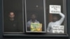 FILE - Three asylum seekers gesture to protesters rallying outside in their support, from their hotel room where they have been detained in Melbourne, Australia, June 13, 2020.