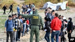 FILE - A U.S. Border Patrol agent directs asylum-seekers waiting between the double fence along the U.S.-Mexico border near Tijuana, Mexico, May 8, 2023, in San Diego, California. 