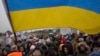FILE - Ukrainian volunteer Oleksandr Osetynskyi, 44 holds a Ukrainian flag and directs hundreds of refugees after fleeing from the Ukraine after arriving at the border crossing in Medyka, Poland, March 7, 2022.