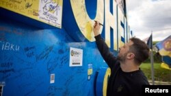 Ukraine President Volodymyr Zelenskiy signs a road sign in Donetsk region, Ukraine, April 19, 2024. (Ukrainian Presidential Press Service/Handout via Reuters)