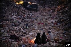 FILE - Members of a family keep warm next to a fire as they follow a rescue team searching for their relatives among destroyed building in Antakya, Turkey, on Feb. 15, 2023.