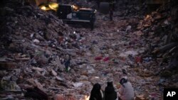 FILE - Members of a family keep warm next to a fire as they follow a rescue team searching for their relatives among destroyed building in Antakya, southern Turkey, Feb. 15, 2023.
