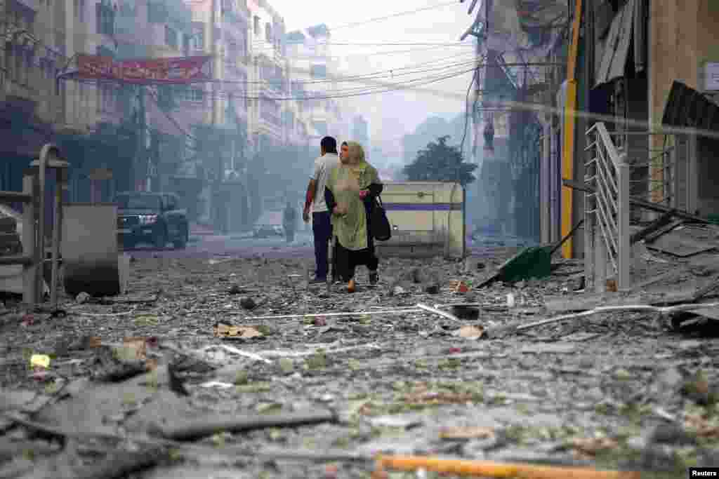 A Palestinian woman walks on a debris-strewn street near the Watan Tower in Gaza City which was destroyed in Israeli strikes, Oct 8, 2023.