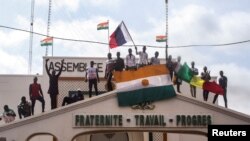 Men hold Niger and Russian flags as they gather with thousands of anti-sanctions protesters in support of the putschist soldiers in the capital Niamey, Niger, Aug. 3, 2023.
