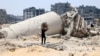 A Palestinian child transporting pieces of wood walks past a building destroyed by Israeli bombardment in Gaza City on May 3, 2024.