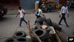 FILE - People pass a barricade that closes the entrance for vehicles after 6 p.m. erected by the Bwa Kale movement, an initiative to fight gangs seeking to take control of the neighborhood, in the Canape Vert area of Port-au-Prince, Haiti, May 31, 2023.