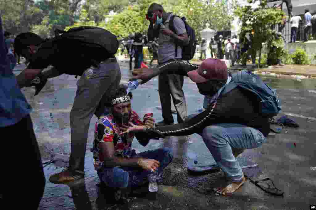A protester helps another after police fired teargas to disperse them before they stormed Prime Minister Ranil Wickremesinghe's office in Colombo, July 13, 2022.