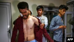 Jurnalis Afghanistan Nematullah Naqdi (kiri) tampak merasa kesakitan ketika dibantu oleh rekannya untuk mengenakan baju setelah ia dilepaskan Taliban dari tahanan pada 8 September 2021. Taliban menangkap Naqdi dan rekannya saat mereka meliput sebuah protes di Kabul. (Foto: AFP)