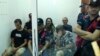 Sejumlah petugas polisi menjaga Mikhail Zorin (kiri, duduk), Svetlana Timofeeva (tengah, belakang), dan Fedir Alpatov (duduk, kanan) dalam persidangan di pengadilan Elbasan, Albania, pada 24 Agustus 2022. (Foto: AP/Franc Zhurda)