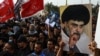 Pendukung ulama Syiah Muqtada al-Sadr membawa potret dirinya saat mereka berkumpul di kota Nasiriyah di Provinsi Dhi Qar selatan Irak, 12 Agustus 2022. (Foto: AFP)
