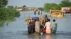 Warga berjalan melintasi jalanan yang tergenang banjir dengan barang-barang mereka, menyusul hujan lebat yang melanda Suhbatpur, Pakistan, 28 Agustus 2022. (Reuters/Amer Hussain)