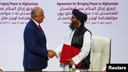 FILE - Mullah Abdul Ghani Baradar, leader of the Taliban delegation, and Zalmay Khalilzad, U.S. envoy for peace in Afghanistan, shake hands after signing an agreement between members of Afghanistan's Taliban and the U.S. in Doha, Qatar, Feb. 29, 2020.