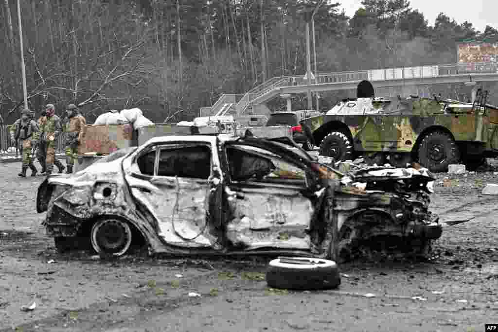 Soldiers walk near a car that was destroyed by recent shelling on a check-point in the city of Brovary outside Kyiv, March 1, 2022.