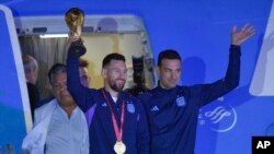 Pesepak bola Argentina Lionel Messi memegang trofi Piala Dunia FIFA saat ia keluar dari pesawat bersama pelatih Lionel Scaloni, di Buenos Aires, Argentina, Selasa, 20 Desember 2022. (AP Photo/Gustavo Garello)