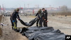FILE - Ukrainian soldiers collect bodies of civilians killed by the Russian forces at the destroyed bridge in Irpin close to Kyiv, Ukraine, March 31, 2022.