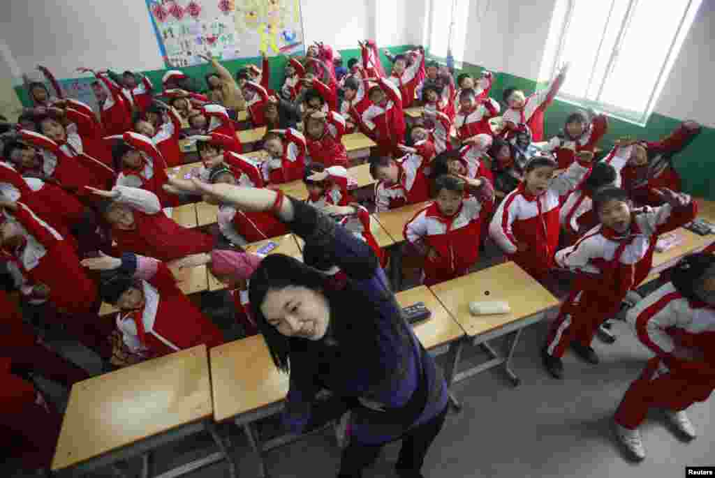 A teacher leads her students doing body exercises during class break in a classroom on a foggy day in Jinan, Shandong province, January 14, 2013.