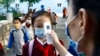 Seorang guru mengukur suhu tubuh seorang siswi untuk membantu mengekang penyebaran virus corona sebelum memasuki Sekolah Dasar Kim Song Ju di Distrik Pusat di Pyongyang, Korea Utara. (Foto: AP)