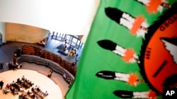 FILE - A Native American flag hangs above American Indian advocates as they contest a Paris auction house's upcoming auction of Native American remains and sacred objects, at the Smithsonian National Museum of the American Indian in Washington, May 24, 2016.