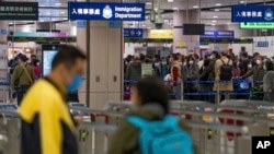 Pemudik yang memakai masker berbaris di loket imigrasi di stasiun Lok Ma Chau setelah dibukanya kembali perbatasan lintas negara dengan China daratan, di Hong Kong, Minggu, 8 Januari 2023. (Foto: AP)