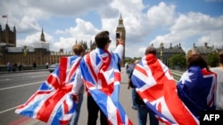 Warga berjalan di sekitar Jembatan Westminster menuju Menara Ratu Elizabeth (Big Ben) dan Gedung Parlemen Inggris dengan membalut diri dengan bendera Inggris di pusat kota London, 26 Juni 2016. (Foto: dok).