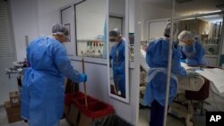 Cleaning worker Anthoula Dimitra Pagouni, 30, uses a stick to press biohazard waste as medical staff examine a COVID-19 patient in an ICU of the Sotiria Thoracic Diseases Hospital in Athens, Jan. 18, 2021