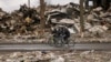 Sejumlah pria tampak mengayuh sepeda melewati gedung-gedung apartemen yang hancur di Borodyanka, Ukraina, pada 6 April 2022. (Foto: AP/Vadim Ghirda)