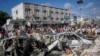 Orang-orang berjalan di sekitar puing-puing di lokasi ledakan bom mobil di Mogadishu, Somalia, 30 Oktober 2022. (Foto: Farah Abdi Warsameh/AP)