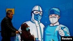 지난달 27일 중국 베이징 시내 방역 포스터 앞으로 휠체어를 탄 시민이 마스크를 쓴 채 지나가고 있다. (자료사진)