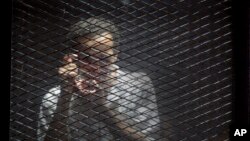 FILE - Egyptian photojournalist Mahmoud Abu Zeid, known by his nickname Shawkan, gestures in a soundproof glass cage inside a makeshift courtroom in Tora prison in Cairo, Egypt, July 28, 2018. 