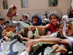 FILE - In this April 13, 2017 photo, Yemenis present documents in order to receive food rations provided by a local charity, in Sana'a, Yemen.