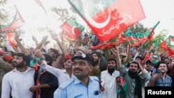 Seorang petugas polisi bereaksi ketika para pendukung Perdana Menteri Pakistan Imran Khan, ketua partai politik Pakistan Tehreek-e-Insaf (PTI), mengibarkan bendera saat ia mendarat dari helikopter di Islamabad, Pakistan, 27 Maret, 2022. (Foto: Reuters)