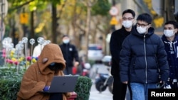 Seorang wanita yang mengenakan masker melihat laptopnya di jalan, saat wabah COVID-19 masih terus terjadi di Shanghai, China, 14 Desember 2022. (Foto: Reuters)