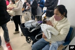 Seorang perempuan menggendong anaknya di Rumah Sakit Anak di Beijing, Rabu, 14 Desember 2022. (Foto: AP)