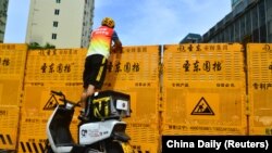 A courier stands on an electric bike to make a delivery over a barricade amid lockdown measures to curb the coronavirus disease outbreak in Sanya, Hainan province, China August 6, 2022.