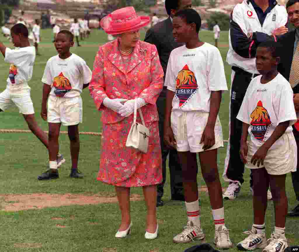 Britain's Queen Elizabeth talks with young cricketers while on a visit to Alexander Township, north of Johannesburg, South Africa Thursday November 11 1999. The Queen is on a state visit ahead of the Commonwealth Heads of Government Meeting starting Friday in Durban. (Photo by THEMBA HADEBE / AP POOL / AFP)