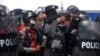 Seorang perwira polisi membidik senjata ke arah para pedemo yang memprotes kudeta militer dan menuntut pembebasan pemimpin Myanmar terpilih, Aung San Suu Kyii di Naypyitaw, Myanmar, 9 Februari 2021. (Foto: Stringer/Reuters)