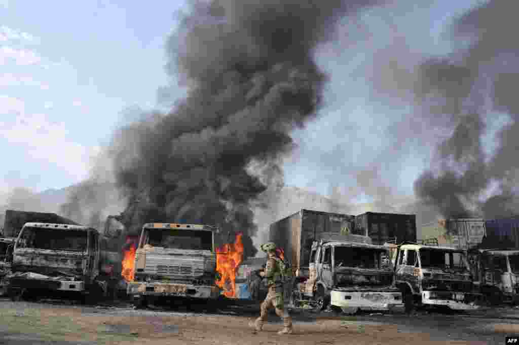 Seorang tentara AS melewati truk yang terbakar akibat serangan bom bunuh diri di Torkham, Nangarhar, Afghanistan.