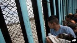 FILE - A member of the Central American migrant caravan, holding a child, looks through the border wall toward a group of people gathered on the U.S. side, as he stands on the beach where the border wall ends in the ocean, in Tijuana, Mexico, April 29, 2018. 