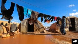 FILE - A woman hangs laundry in a flooded refugee camp in Idlib province, Syria, Dec. 21, 2021.