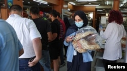 FILE - People queue as a woman carries several loafs of bread at a bakery in Beirut, Lebanon, June 29, 2022.