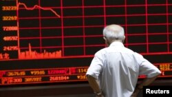 Seorang investor mengamati papan elektronik yang menampilkan indeks-indeks di Beijing, China (7/7).