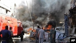 Quelques personnes se rassemblent autour des bâtiments en feu après une attaque à la bombe dans la banlieue de Sayyida Zeinab, à Damas, Syrie, 11 juin 2016. 