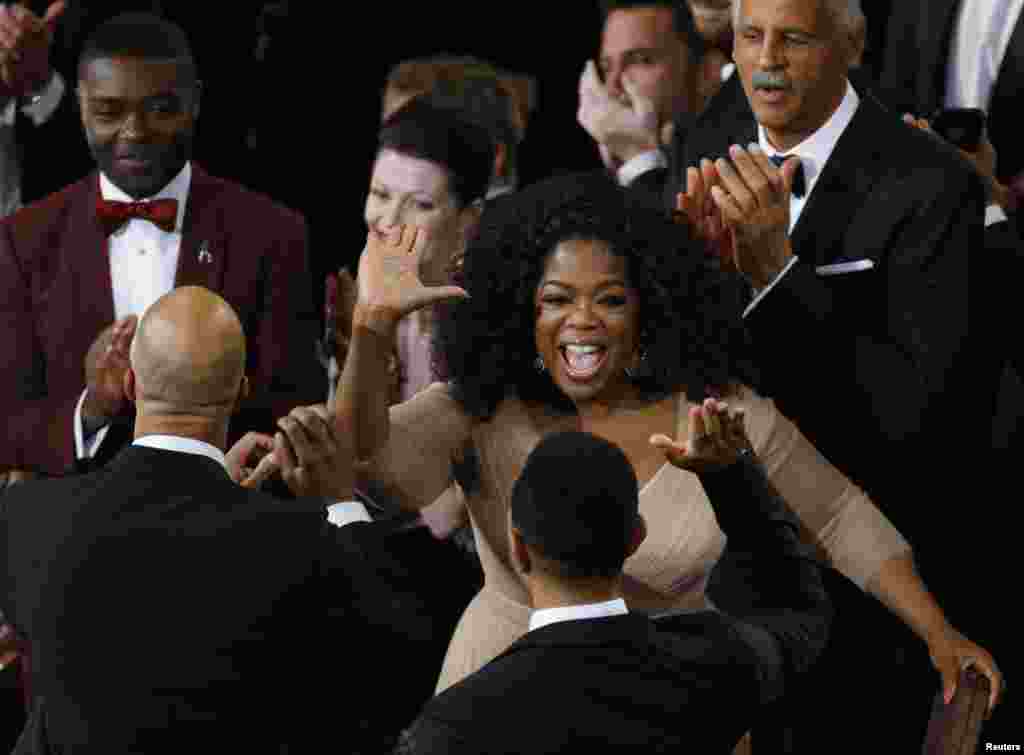 Ophra Winfrey (C) félicite John Legend (en bas D) et Commun (en bas G), pendant que l'acteur David Oyelowo (haut à gauche) regarde, après que "Glory" du film "Selma" a remporté l'Oscar de la meilleure chanson originale lors de la 87e Oscars à Hollywood, en Californie 