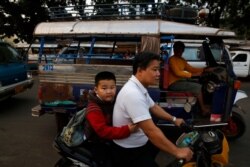 FILE - A Lao boy holds his father as he goes to school on a scooter, in the capital Vientiane, Laos.