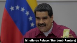 FILE - Venezuela's President Nicolas Maduro holds a 100,000 bolivar note as he speaks during a meeting with ministers in Caracas, Venezuela, Nov. 1, 2017. 