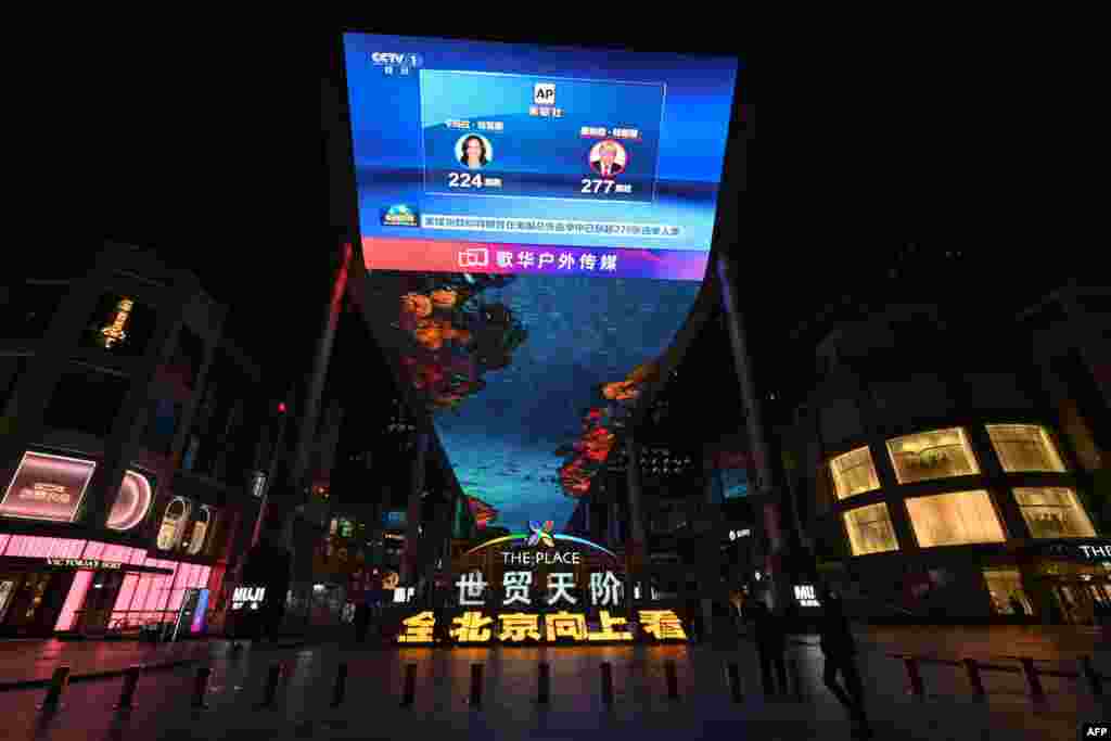 People walk past a screen broadcasting news on the US election results outside a mall in Beijing on Nov. 6, 2024.