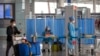 A man pushes his luggage past workers in protective suits as they wait to take the temperature of travelers at Beijing Capital International Airport in Beijing, March 6, 2020.