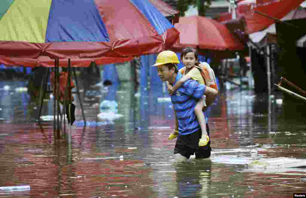 Seorang laki-laki menggendong seoranga anak perempuan di punggungnya berjalan di tengah banjir akibat hujan deras menghantam Provinsi Changsha, Hunan, China. 
